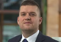 Dan Proud, Director, Infrastructure, UK, outside in front of a blurred brown background featuring a building and mix of natural and urban elements.