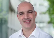 Hans Weemaes, Director, Sustainability, Asia, standing outside in front of an outdoor urban setting, featuring modern architectural elements with clean lines. There are hints of greenery, suggesting some trees or plants.