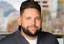 Jonathan Elden, Vice President, US,  standing outside in front of buildings featuring an urban cityscape with a mix of architectural styles. The scene includes some windows and red features, adding a touch of color.