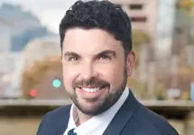 Michael Hardman, Vice President,  standing outside featuring an urban cityscape with tall buildings and a mix of architectural styles. The scene includes some trees with autumn foliage, adding a touch of color. 