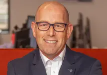 Portrait of Philip Matthews, Managing Director, Ireland, outside in front of a blurred brown background featuring a building and mix of natural and urban elements.