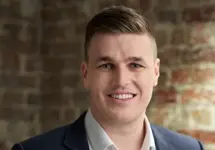 Portrait of Danny Waters, Associate Director, Standing against brown brick wall in blue suit